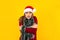 Young latin woman with frozen face and cold in Santa hat Christmas sweater and warming up holding arms crossed on yellow backgroun