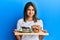 Young latin woman holding cake sweets and cookies clueless and confused expression