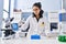 Young latin woman scientist writing on notebook holding pills at laboratory