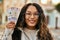 Young latin woman smiling happy holding colombia pesos banknotes at the city