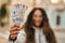 Young latin woman smiling happy holding colombia pesos banknotes at the city