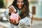 Young latin woman smiling happy saving euro coin in the piggy bank at the city