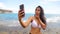 Young Latina girl takes selfies on the beach and sticks out her tongue making grimances and funny faces