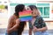 Young lesbian couple kissing and hiding behind a rainbow flag outdoors.