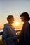 Young lesbian silhouetted couple having romantic moment while listening to music sharing one same earphones, standing on