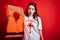 Young lifeguard woman holding rescue lifejacket over red background scared in shock with a surprise face, afraid and excited with