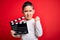 Young little boy kid filming video holding cinema director clapboard over isolated red background annoyed and frustrated shouting