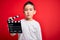 Young little boy kid filming video holding cinema director clapboard over isolated red background with a confident expression on