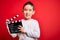 Young little boy kid filming video holding cinema director clapboard over isolated red background with a happy face standing and