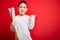 Young little boy kid looking at turist city destination map over red isolated background pointing and showing with thumb up to the