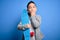 Young little boy kid skateboarder holding modern skateboard over blue isolated background cover mouth with hand shocked with shame