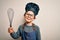 Young little caucasian cook kid wearing chef uniform and hat using manual whisk with a happy face standing and smiling with a