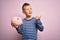 Young little caucasian kid banking money on piggy bank as wealth savings over pink background pointing and showing with thumb up