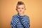 Young little caucasian kid with blue eyes wearing nautical striped shirt over yellow background shocked covering mouth with hands