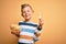 Young little caucasian kid eating unheatlhy potatoes crisps chips over yellow background with a happy face standing and smiling