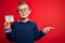 Young little caucasian kid wearing glasses holding paper note with question mark sign very happy pointing with hand and finger to