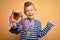 Young little caucasian kid wearing winner medals and victory award trophy over yellow background very happy and excited, winner