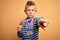 Young little caucasian winner kid wearing award competition medals over yellow background pointing with finger to the camera and