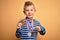 Young little caucasian winner kid wearing award competition medals over yellow background with surprise face pointing finger to