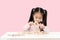 Young little cute asian girl build a house from wooden block construction, wood toy, jenga house on desk in isolated pink