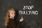 Young little cute schoolgirl scared sad writing the words stop bullying text written with chalk