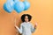 Young little girl with afro hair holding ice cream and blue balloons making fish face with mouth and squinting eyes, crazy and