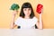 Young little girl with bang holding broccoli and red pepper skeptic and nervous, frowning upset because of problem