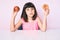 Young little girl with bang holding red apple and donut sitting on the table clueless and confused expression