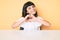 Young little girl with bang wearing casual clothes sitting on the table smiling in love doing heart symbol shape with hands