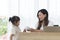 Young little girl bring cup of coffee to her mother, while young mother working on desk using laptop computer during work from hom