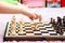 Young little girl, child playing chess, chessboard side view, hand moving a chess piece, about to grab it, closeup. Making a move