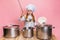 Young little girl in white cook uniform and huge chef& x27;s hat at kids kitchen with big pans isolated on pink studio