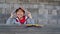 Young little latino boy latino holding a yellow book on his head on brick background with pencils over the desk and having fun and