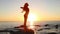 A young long-haired girl making yoga practice standing on a rock by the sea. Summer, sunset. Woman`s silhouette