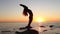 A young long-haired girl making yoga practice standing on a rock by the sea. Summer, sunset. Woman`s silhouette