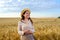 Young long-haired woman in a straw hat holds stalk of wheat and smiling in field