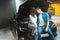 Young lovely couple handsome man and beautiful woman sitting on the vehicle bonnet hugging in electric car dealership center,