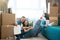 Young lovely couple man and woman looking satisfied sitting on the floor hugging during moving to new apartment unpacking boxes