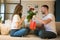 Young lovely couple sitting on the sofa, man surprising wife with flowers and gift on saint valentine`s day, happy unniversary