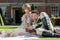 Young lovers dressed in vintage clothing sitting on picnic blanket. Gentleman reading to his lover from a book of poems