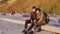 Young loving couple with backpacks sits on log on sandy beach