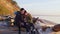 Young loving couple with backpacks sits on log on sandy beach