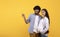 Young loving indian pregnant couple pointing aside at copy space, showing great offer or promo, yellow background