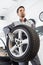 Young maintenance engineer carrying tire in automobile store