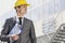 Young male architect with clipboard looking away outside office building