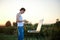 Young male artist, standing by easel, drawing portrait on canvas on green field in summer during sunset. Painting workshop in