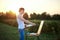 Young male artist, standing by easel, drawing portrait on canvas on green field in summer during sunset. Painting workshop in