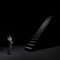 Young male businessman looking up in front of a big long stairs. Dark background. 3D illustration