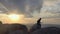 A young male climber walks along the top of a mountain range and jumps over a chasm at sunset.