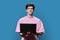 Young male college student using laptop, blue background